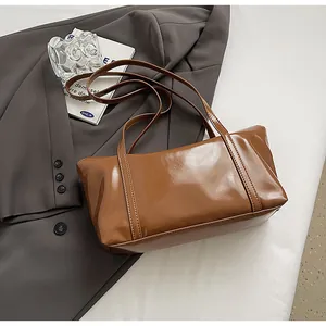 Detail of glossy brown oil wax leather shoulder bag with sleek stitching and handles