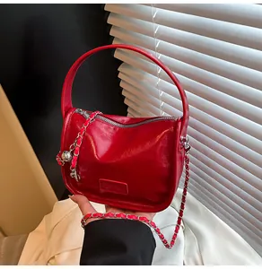 Close-up of vibrant red glossy leather handbag with silver chain strap and metal zipper
