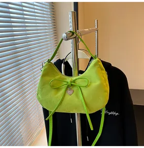 Detail van groene suède handtas met strikdecoratie en hartbedeltje aan een hanger