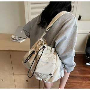 Detail of beige nylon crossbody bag featuring drawstring closure and metal logo pocket