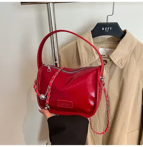 Detail of glossy red handbag with silver chain strap and fashion label on tan trench coat