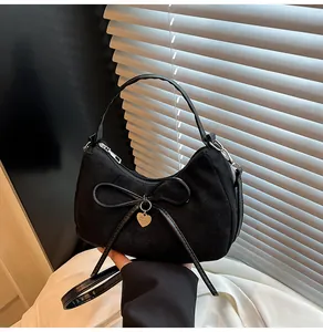 Detailopname van zwarte imitatiesuède tas met strik en gouden hartvormige hanger
