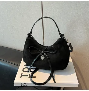 Detail van zwarte suède handtas met lederen strik en hartvormige hanger op boeken