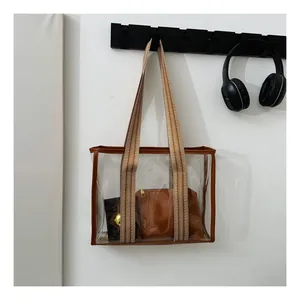 Detail of transparent PVC tote bag with brown leather trim and striped woven strap