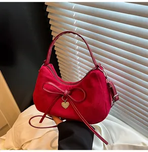 Gedetailleerde close-up van een rode suède handtas met strik en gouden hartje hanger
