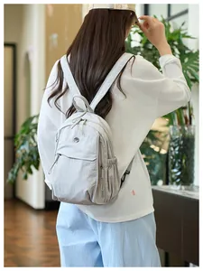 Back view of light grey nylon backpack with side pockets and metal M logo on male model