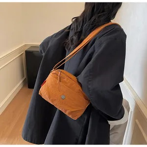 Detail einer dunkelorangefarbenen Nylon-Umhängetasche mit Metall-Logo und Reißverschluss