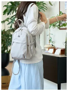 Detail of light gray nylon backpack featuring multi-zipper pockets and water-resistant fabric