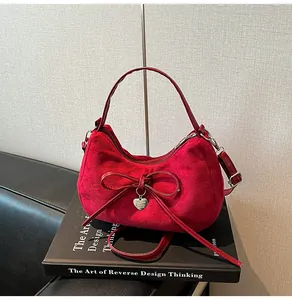 Detailopname van rode suède handtas met strikdecoratie en gouden hartvormige hanger
