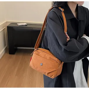 Braune Nylon-Umhängetasche mit Metall-Logo an Modell in stilvollem Innenraum