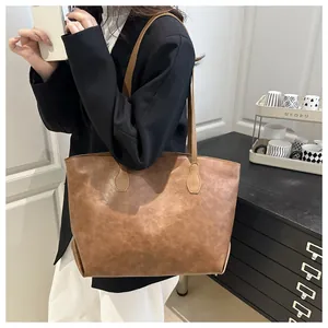 Detail view of a vintage brown faux leather tote bag worn by a model in a black suit