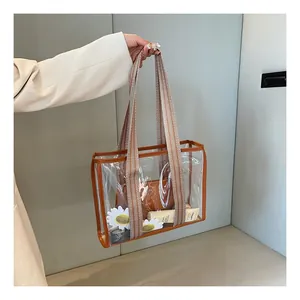 Detail view of transparent PVC tote bag with brown leather trim and striped wide strap
