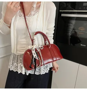 Detalle del bolso Boston de charol rojo con lazo de encaje y adornos metálicos