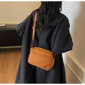 Detail einer orangen Nylon-Umhängetasche mit Reißverschlussfächern und verstellbarem Gurt