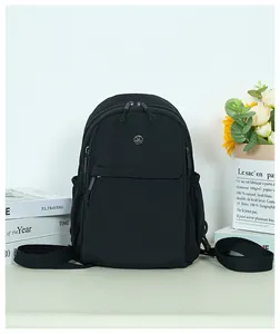 Detail of black nylon backpack featuring a round metal logo and front zipper pocket