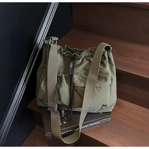 Detail of olive green nylon crossbody bag with drawstring and pockets on wooden stairs