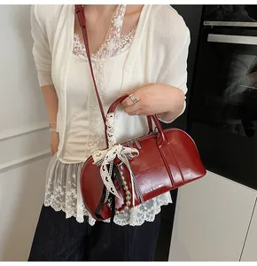 Detalle del bolso Boston rojo oscuro con lazo de encaje y colgante de cuentas metálicas