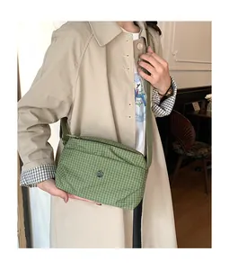 Gros plan d'un sac à bandoulière en toile à carreaux verts avec logo sur un trench beige