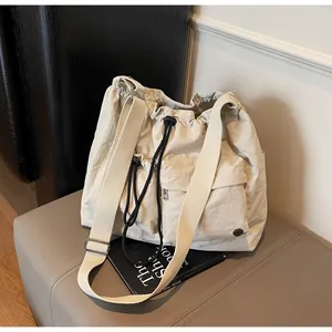 Detail of beige nylon crossbody bag featuring double front pockets and black drawstring cords