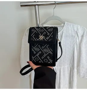 Close-up of black floral embroidery and golden clover clasp on a mini crossbody bag