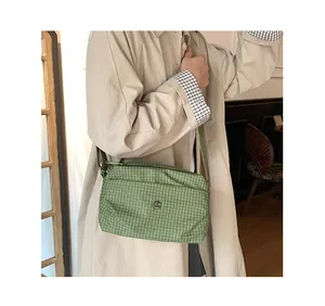 Détail du sac bandoulière en toile à carreaux verts avec logo JM en métal et sangle en tissu