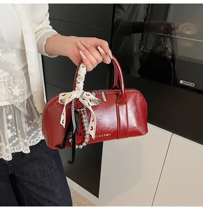 Detalle del bolso de piel brillante burdeos con lazo de encaje y colgante plata