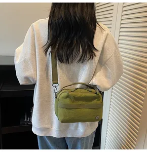 Olive green nylon crossbody bag with adjustable wide strap shown in a street style back view