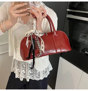 Detalle de bolso burdeos de charol con lazo de encaje y colgante de cuentas
