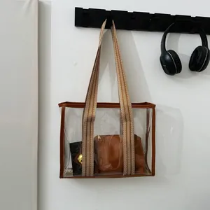 Large transparent PVC tote bag with brown leather trim and striped shoulder strap
