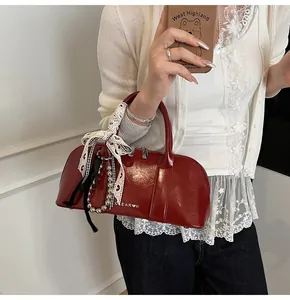 Detalle de bolso de hombro en cuero brillante burdeos con lazo decorativo y colgantes
