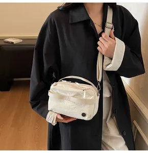 Detail of minimalist cream crossbody bag with textured fabric and top handle on model