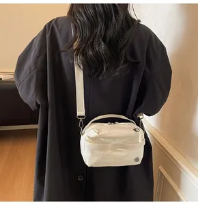 Close-up of cream nylon crossbody bag with adjustable wide strap and round logo detail