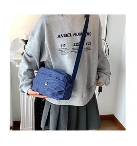 Détail d'un sac bandoulière en toile à carreaux bleus avec sangle réglable et logo rond
