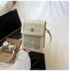 Detailed view of beige embroidered square phone bag with golden clover metal clasp