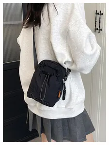 Detail of black nylon drawstring crossbody bag with embossed logo and side woven label