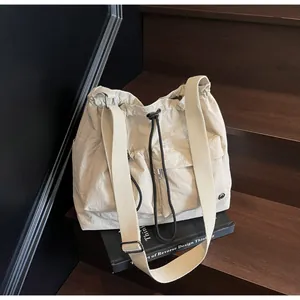 Detail of beige nylon crossbody bag with black drawstrings and large front pockets