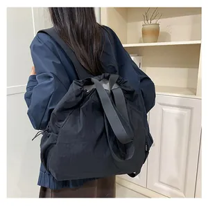 Detail van een grote zwarte nylon schoudertas met trekkoord en merklabel aan de zijkant