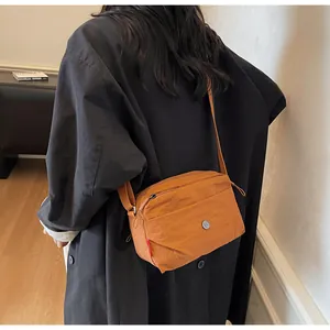 Rückansicht eines Modells mit orangefarbener Nylon-Umhängetasche mit Reißverschlussfächern