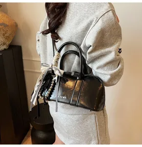 Detalle de bolso negro brillante con lazo de cuadros y colgante de cuentas plateadas