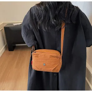 Lässige orangefarbene Nylon-Umhängetasche am Modell mit mehreren Reißverschlussfächern