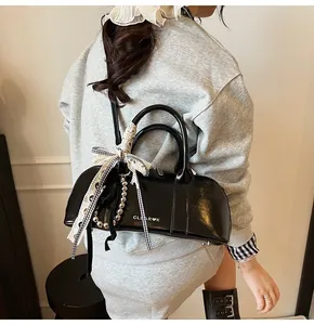 Bolso de hombro negro brillante con lazo y cadena de cuentas sobre un atuendo gris