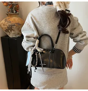 Detalle del bolso bandolera negro brillante con lazo de encaje y colgante de cuentas