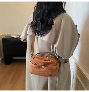 Chic caramel nylon crossbody bag with wide strap and metal logo on a beige trench coat