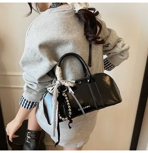 Detalle de bolso Boston negro brillante con lazo de encaje y letras de metal plateado