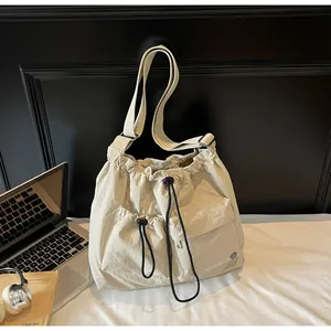 Detail of beige nylon crossbody bag featuring drawstring pockets and wide shoulder strap
