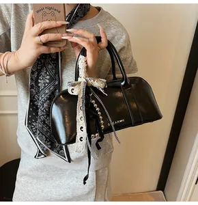 Detalle de bolso Boston negro brillante con lazo de encaje y colgante metálico