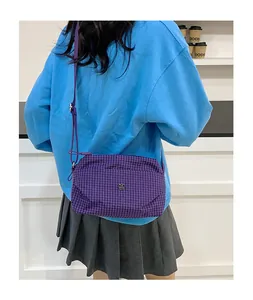 Détail du sac bandoulière en toile à carreaux violets avec logo en métal sur modèle