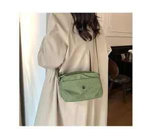 Détail du sac bandoulière en toile à carreaux verts porté par un mannequin en intérieur