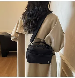 Close-up of black nylon crossbody bag with silver round logo and wide shoulder strap