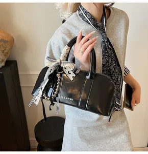 Detalle de bolso de cuero negro con lazo de cuadros y colgante de perlas en una modelo